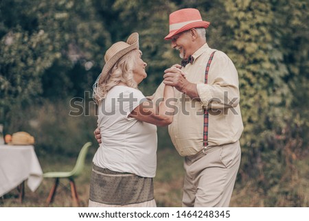 A grandfather with happy eyes looks grandmother in the eyes. Youth memories. The concept of a happy old age. Portrait of oldies who are dancing in the garden Royalty-Free Stock Photo #1464248345