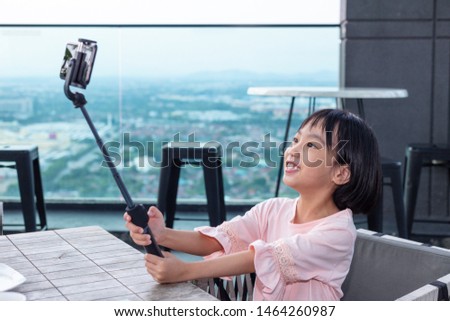 Asian Little Chinese Girl taking selfie with smartphone on selfie stick in the outdoor cafe