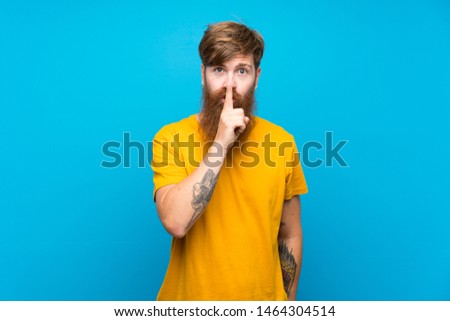 Redhead man with long beard over isolated blue background showing a sign of silence gesture putting finger in mouth