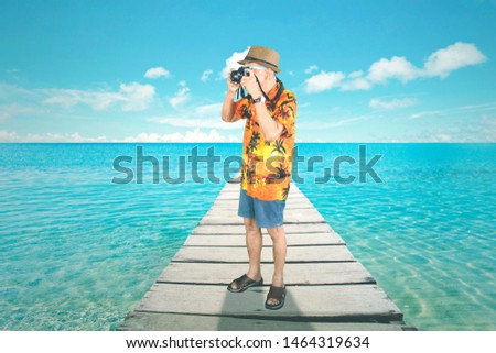 Picture of elderly man using a digital camera to take a photo on the beach, Shot in the dock bridge