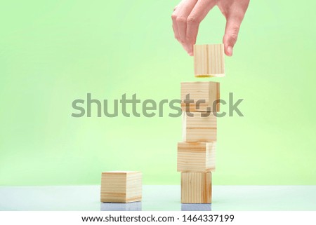 Hand build a stack of wooden block toy on the table over green background