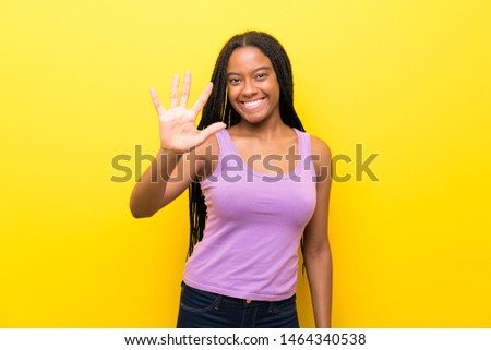 African American teenager girl with long braided hair over isolated yellow wall counting five with fingers