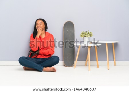 African American skater teenager girl with braided hair sitting on the floor laughing