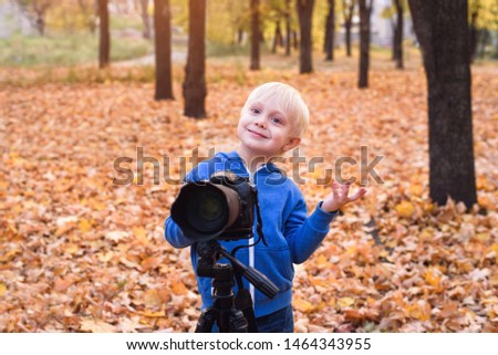Portrait of a little blond boy with a large DSLR camera on a tripod. Photo session in the autumn park