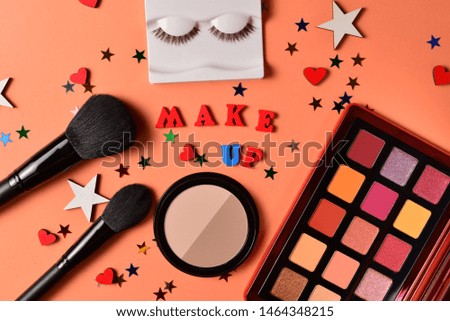 Make up text on an orange background. Professional trendy makeup products with cosmetic beauty products,  eye shadows, eye lashes, brushes and tools.