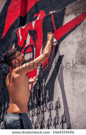 Young graffiti artist painting with sprays a wall in the street