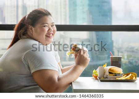 Picture of fat woman smiling at the camera while eating a hamburger in the restaurant