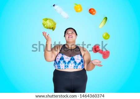 Picture of overweight woman wearing sportswear while juggling dumbbell and foodstuff 