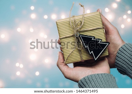 Woman's hands hold christmas or new year decorated gift box. Toned picture. Blurred lights in the background. Happy New Year 2020