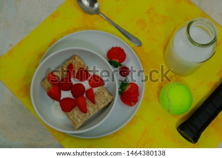 Strawberries and cereal for a July breakfast. A tennis ball and racket handle complete the picture.