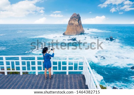 Rear view of young woman taking a photo of beautiful seascape while standing in the Tanjung Papuma beach