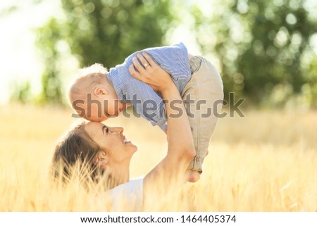 Beautiful woman playing with her little son in wheat field on summer day