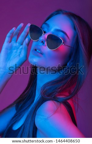 Very beautiful girl in sunglasses. Gorgeous brunette with plump natural lips. Portrait of a girl, model shot on a long exposure in the studio with color filters. Portrait, fashion, beauty, glow. Woman