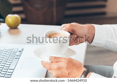 Young businessman working at laptop computer with hot coffee in hand.