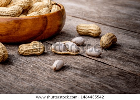 Peeled and unpeeled peanut or goober  in wooden bowl and spilling out on the rustic wood table. Healthy food concept.