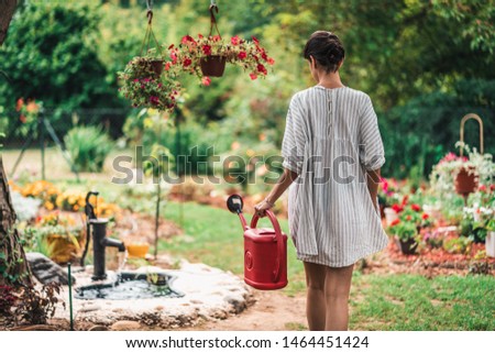 Beautiful young female in garden taking care of plants and flowers. Pretty girl taking care of garden. Watering flowers from watering can in summer time Royalty-Free Stock Photo #1464451424