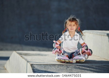 Cute little girl with roller skates outdoors sits on the ramp for extreme sports.