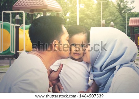 Close up of young parents kissing their daughter while playing in the playground