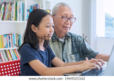 Picture of little girl learning to use a laptop computer with her grandfather in the library