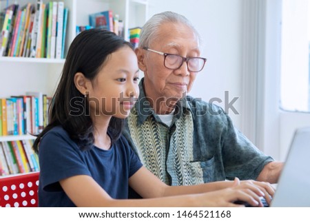 Picture of little girl and her grandfather using a laptop computer together in the library