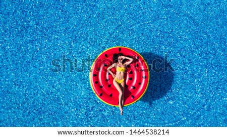 Young woman relaxing on watermelon in hotel resort pool. Top view of rich girl floating with fruit mattress drinking cocktail.