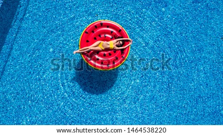 Young woman relaxing on watermelon in hotel resort pool. Top view of rich girl floating with fruit mattress drinking cocktail.