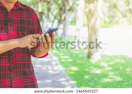 Men wearing red striped shirts use mobile phones in the park.