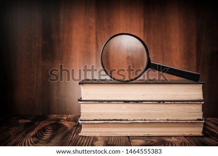 A magnifying glass on a stack of old books on a wooden table.