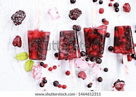 Homemade ice lollies made of wild berries lie on a bright wooden surface with berries and mint leaves - refreshing healthy organic ice in the hot summer as background
