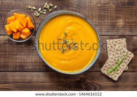 Pumpkin soup with cream on wood texture, top view. Vegan food.