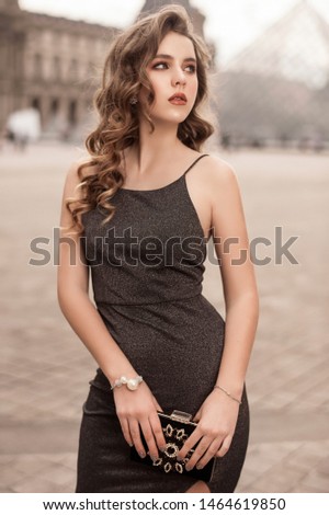 Very beautiful young girl with long blond hair in Paris near the Elfel Tower in a luxurious gray dress
