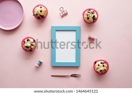 Top view of mock up photo frame with blank space for text on pink background. Chocolate chips muffins on desk. Food menu or recipe concept.