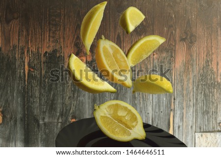  pieces of lemon flying in the air on the black plate with a wooden background Royalty-Free Stock Photo #1464646511