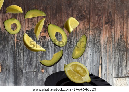  pieces of lemon and avocados flying in the air on the black plate with a wooden background Royalty-Free Stock Photo #1464646523