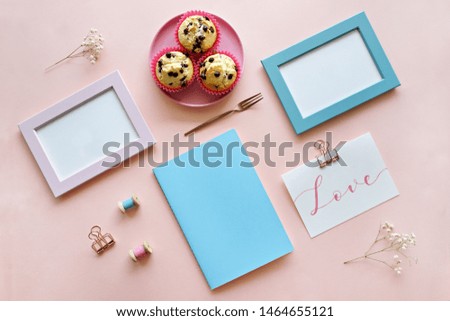 Top view of mock up photo frame with blank space for text on pink background. Chocolate chips muffins, notebook and card on desk. 