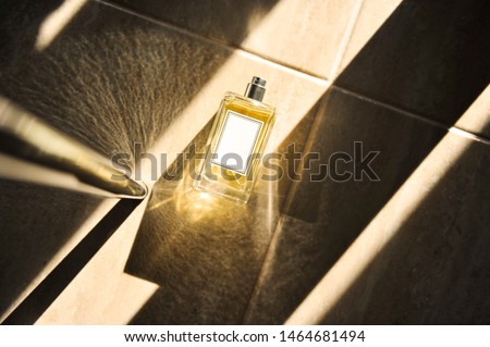 Bottle of summer perfume filled with citrus components on floor. Shadows and light dancing. White label on glass for fragrance name. Scent for women and men. Strong shadows. Banner with copy space. Royalty-Free Stock Photo #1464681494