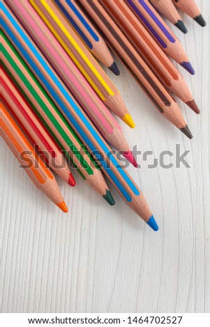 Top view of several colored pencils for school diagonally on white wooden background in vertical with copy space