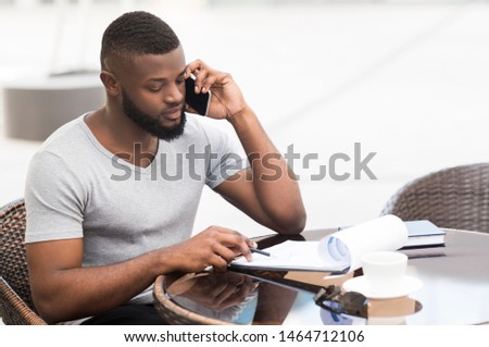 Concentraed african american businessman working with important data in cafe and speaking by phone, copy space