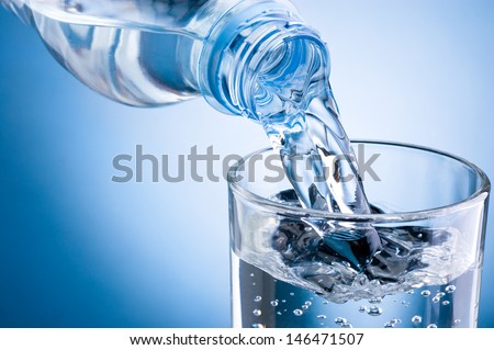 Pouring water from bottle into glass on blue background Royalty-Free Stock Photo #146471507