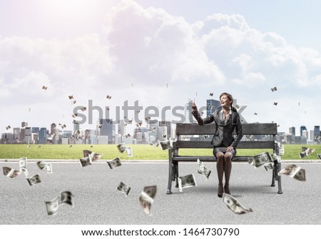 Business woman taking selfie photo or chatting with smartphone. Attractive girl using mobile phone on wooden bench. Mobile marketing and communication. Cityline panorama with falling money banknotes