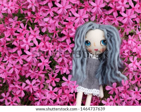 A handmade little girl doll with long hair in beautiful dress on feild of blooming flower background. unique doll. lovely pink flower background