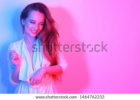 Fashion portrait of young elegant girl. Colored neon background, studio neon shot. Beautiful brunette woman. White dress and long hair. Club, party, the girl looks away, copy space