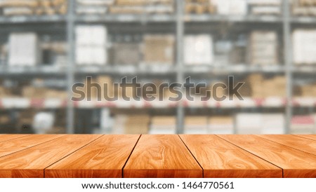 Wood table in warehouse storage blur background with empty copy space on the table for product display mockup. Hardware goods distribution and industrial logistics concept.