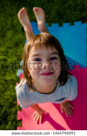 girl of European appearance 7 years old in a gray T-shirt and dark hair doing exercises, doing stretching, yoga, sports against the backdrop of the sun on the green grass, on the lawn, sports concept