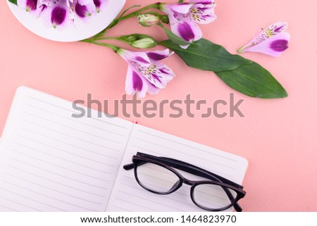 View from above. Fragrant tea in a white cup, beautiful flowers, a pink background, a notebook with a pen and glasses. Office.