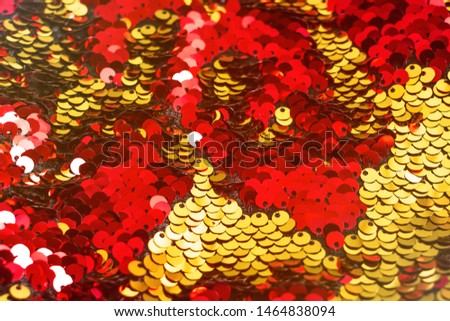 Background of sequin. Fashion shiny fabric. Scales of round sequins. Festive abstract glittery background. Red and golden two-sided sequins. Selective focus. 