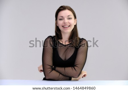 Portrait of a pretty beautiful fashionable adult girl with beautiful brunette hair in a black dress. Sits at the table directly in front of camera, talking demonstrating different poses and emotions
