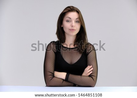 Portrait of a pretty beautiful fashionable adult girl with beautiful brunette hair in a black dress. Sits at the table directly in front of camera, talking demonstrating different poses and emotions