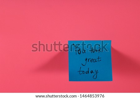 You look great today. Blue sticky note with inspirational quote on neon pink background. Handwritten positive reminder/advice. Concept for confidence, courage and motivation. Sign of moral support.