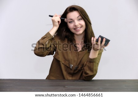 Portrait of a pretty adult brunette girl in a dress on a white background. Sits at the table, talks, explains, with cosmetics in hand, showing different poses and emotions